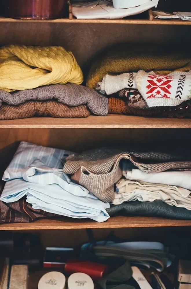 Folded jumpers and shirts stacked on wooden wardrobe shelves
