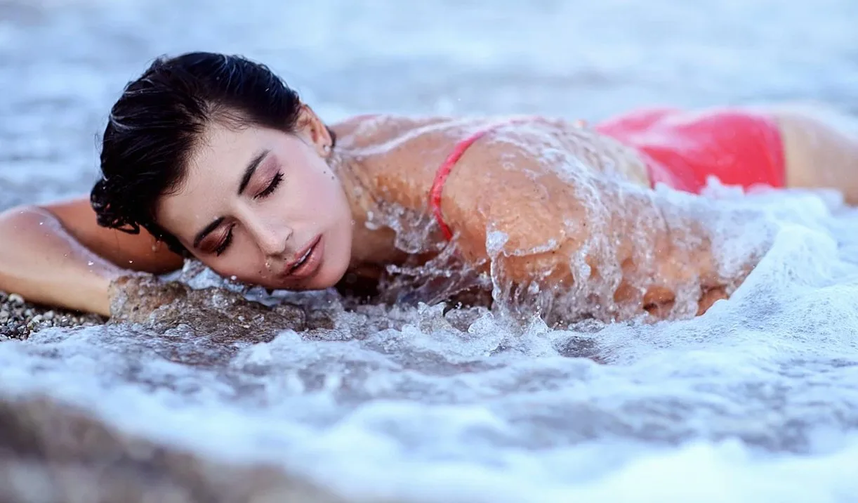 Woman in a red swimsuit resting her face on her arm in foaming seawater
