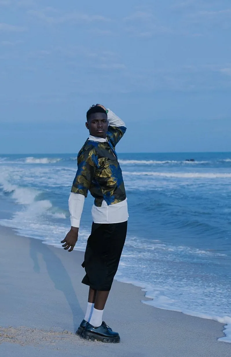 Man in a printed jacket and shorts walking along the water's edge