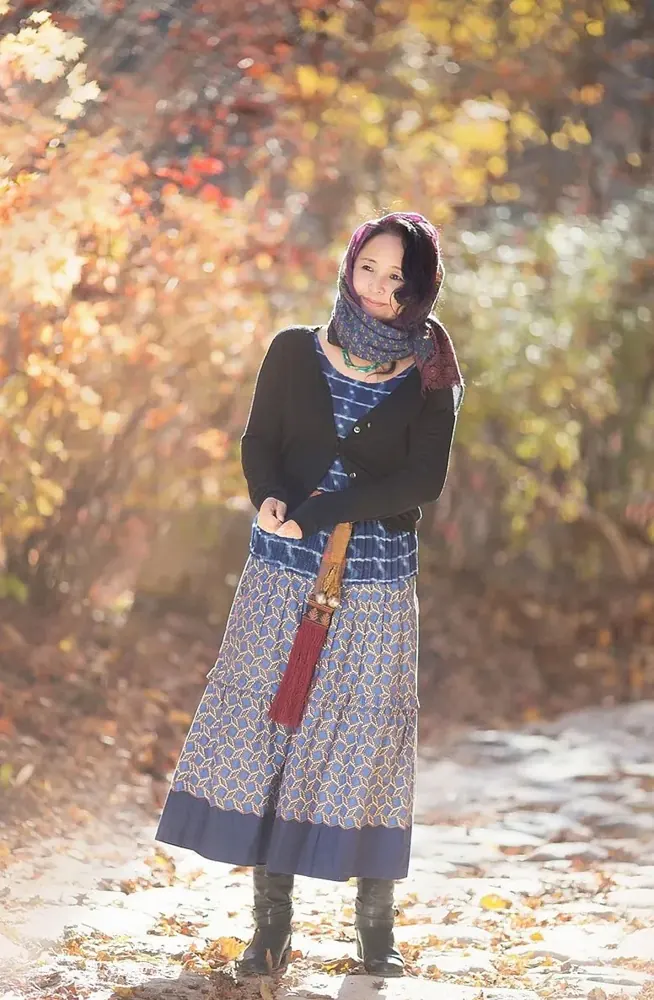 Woman in a scarf and patterned long skirt standing among autumn trees